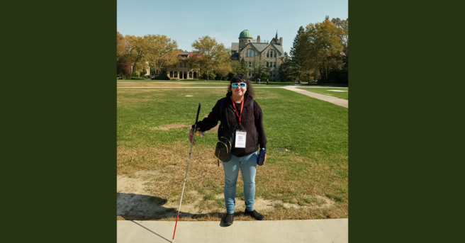 Gabby holding her white cane on a college campus