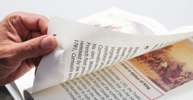 A hand turning the large print page of a book.